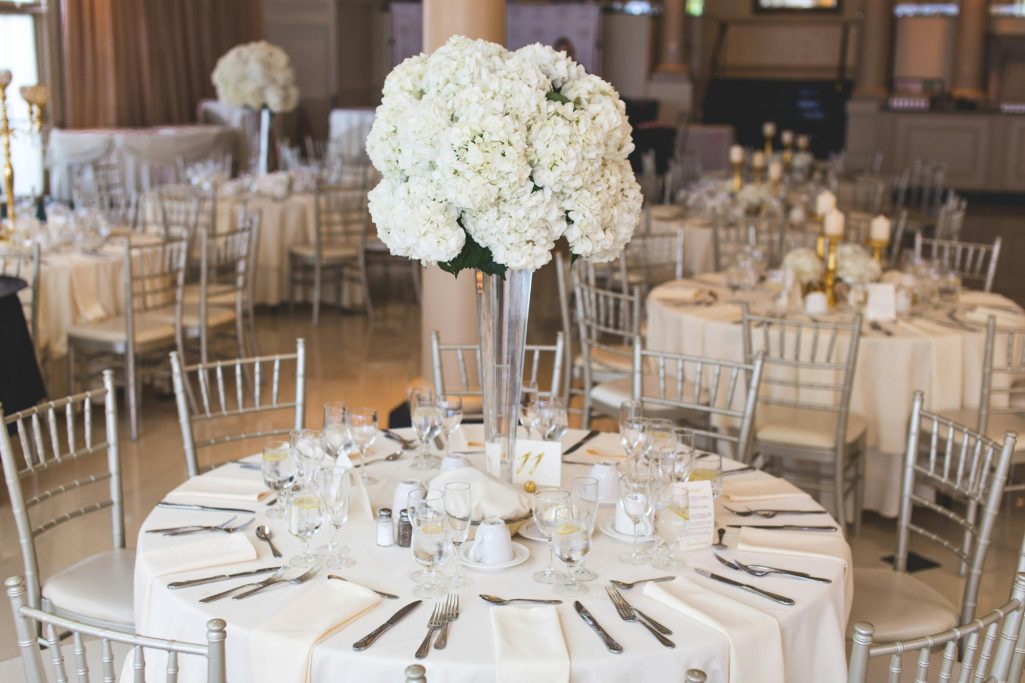 Elegant dining setup with tall white floral centerpieces and gold accents on tables.