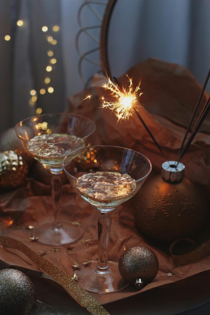 Two sparkling drinks in glasses with festive decorations and a sparkler on a textured surface.