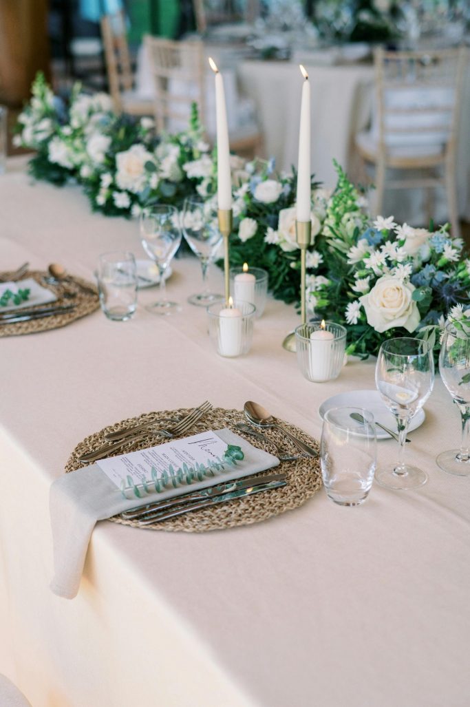 Elegant table setting with floral centerpieces, candles, and menu cards.