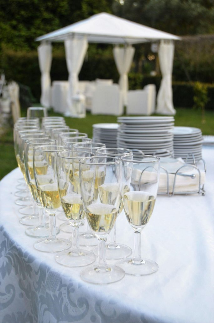 Champagne flutes on a table with white plates and a gazebo in the background.